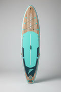 A TIDE TREK stand-up paddleboard standing vertically on cardboard in front of a light blue-gray metal warehouse building under a cloudy sky.